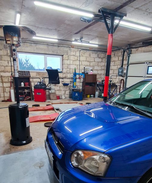Garažas, kuriame montuoja padangas, stovi automobilis subaru, matosi keltuvas, montavimo ir balansavimo staklės